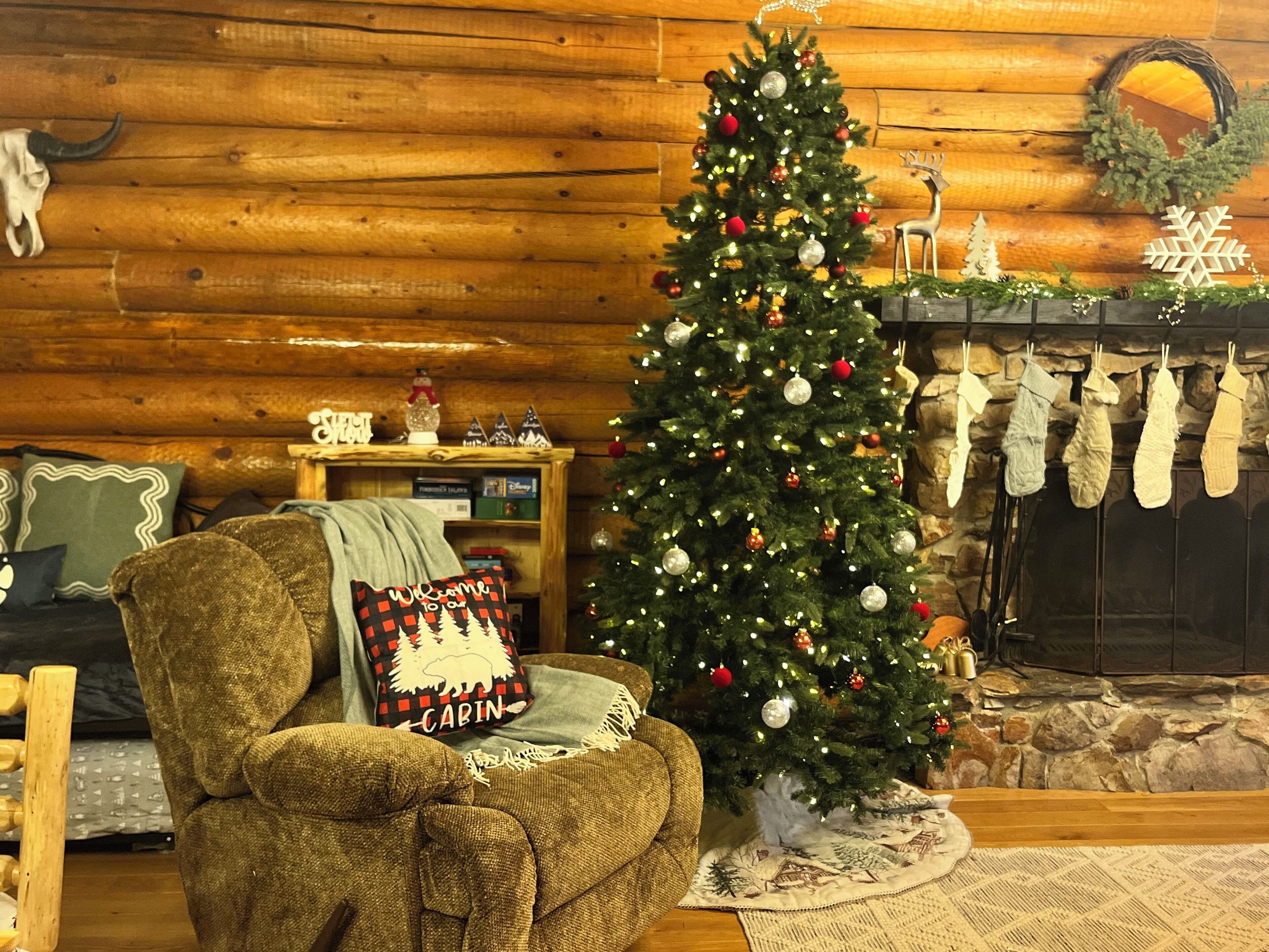 Interior acogedor de una cabaña con un árbol de Navidad decorado, una chimenea con calcetines navideños y una pared de madera rústica.