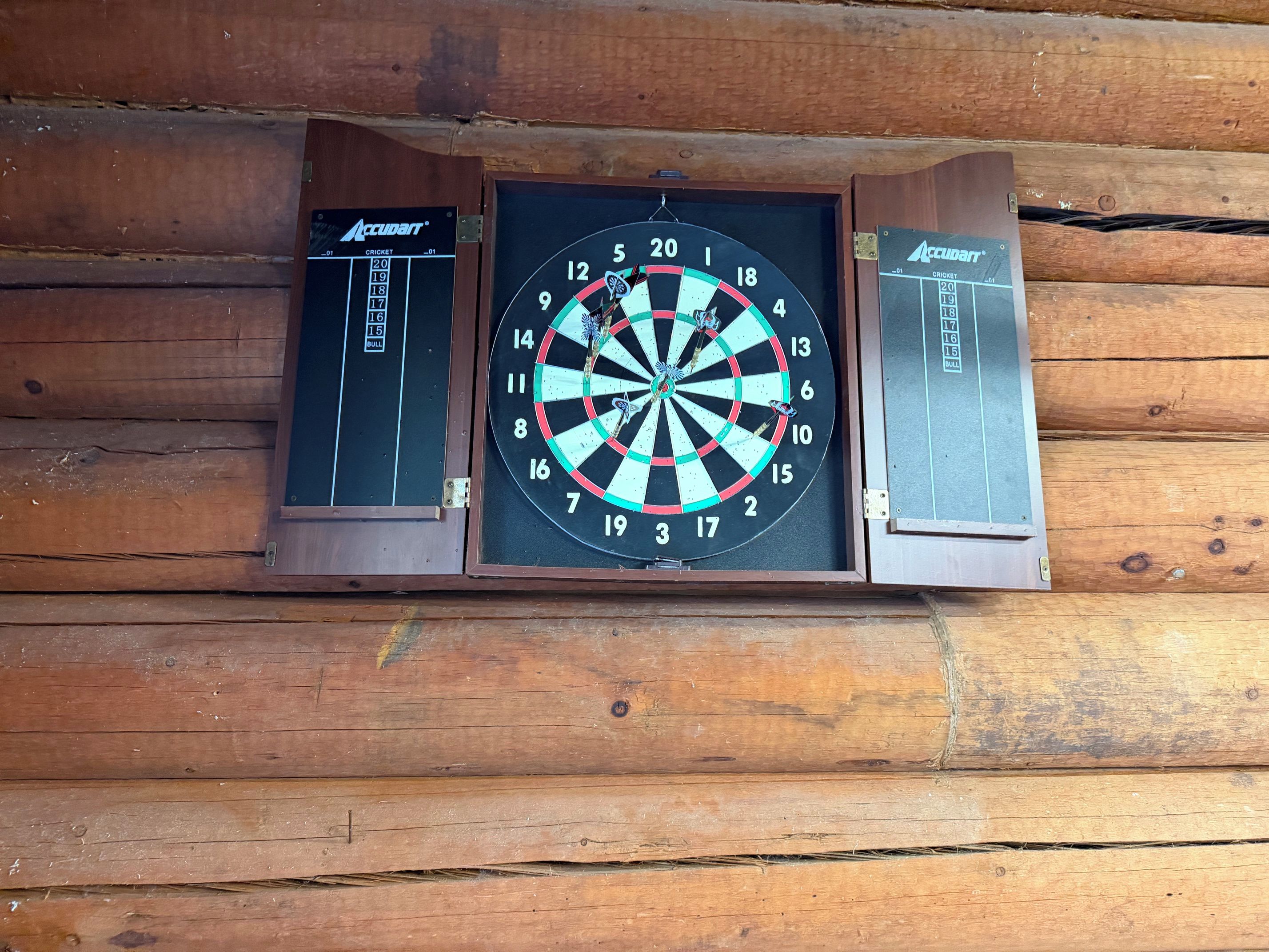 Une cible de fléchettes fixée à un mur en bois, avec un tableau de pointage de chaque côté.