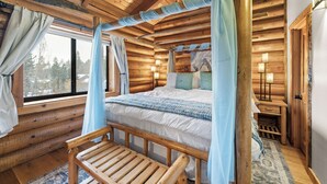 Ein Schlafzimmer in einer Blockhütte mit einem Himmelbett, einer hölzernen Bank und einem großen Fenster mit Vorhängen.