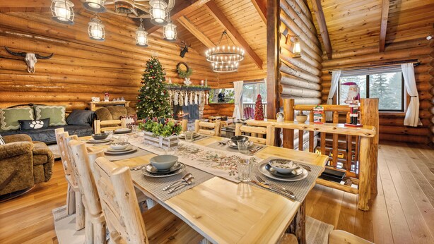 Ein Holzblockhaus-Interieur mit Essbereich, Holzmöbeln, einem Weihnachtsbaum und einem großen Fenster.