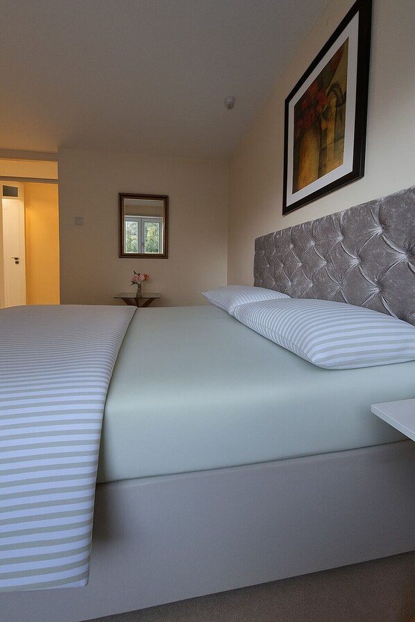 A neatly made bed with striped bedding, a tufted headboard, and a framed picture on the wall. - The terrace (Redbourn)
