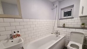 Un baño con paredes de azulejos blancos, una bañera, un inodoro y un lavabo.