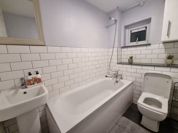 A bathroom with white tiled walls, a bathtub, a toilet, and a sink. - The terrace (Redbourn)