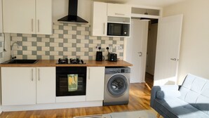 Cocina compacta con horno empotrado, microondas y lavadora, un lavamanos y encimera de madera.