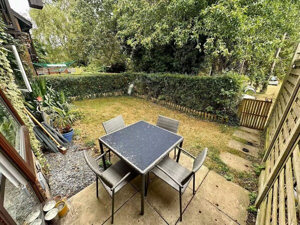 A patio with a table and chairs, surrounded by a garden and a wooden fence.