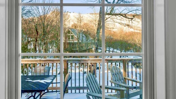 A view through a window with a wooden deck, outdoor furniture, and a house in the background. - Walk to Slopes-Mountain Views-Firepit-Sleeps 10 (Beech Mountain)