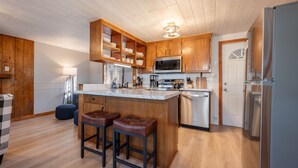 Una cocina moderna con armarios de madera, un refrigerador de acero inoxidable y una zona de bar con taburetes.