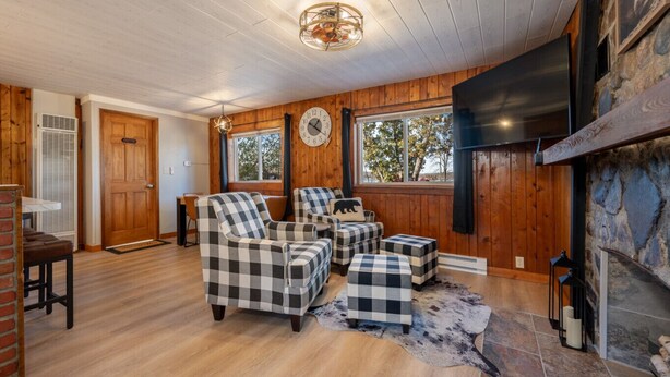 Un salón acogedor con paredes y suelos de madera, chimenea, televisor y mobiliario a cuadros.