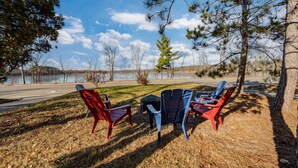 Vista al lago con cuatro sillas Adirondack dispuestas en semicírculo, con vista a un lago tranquilo y un área boscosa.