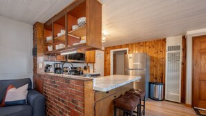 Cocina compacta con pared de ladrillo decorativa, refrigerador de acero inoxidable y un taburete de bar.