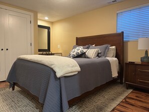 Une chambre bien rangée, avec un lit, des tables de chevet, un miroir et une fenêtre avec des stores.