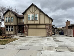 Une maison à deux étages, avec une façade de couleur beige, un garage et un jardin devant.