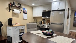 A modern kitchen with white cabinets, a stainless steel refrigerator, a built-in oven, and a coffee machine. - Stay cool in Basement apartment close to Mountain Trails (Sandy)