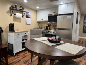 A modern kitchen with white cabinets, a stainless steel refrigerator, a built-in oven, and a coffee machine.