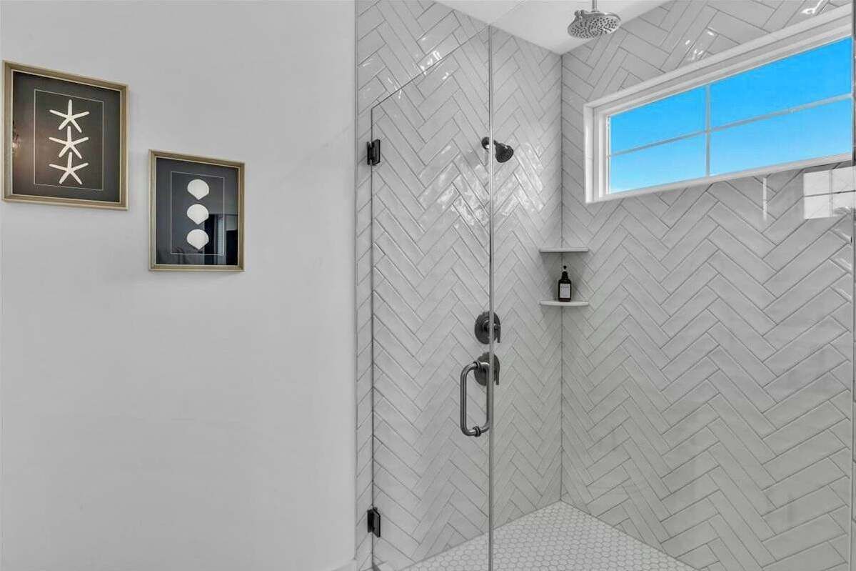 A modern bathroom with a herringbone tile pattern, a glass shower enclosure, and a window providing natural light.