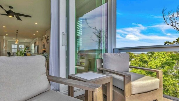 Ein Balkon mit einer Couch und Sesseln, einem Deckenventilator und Blick ins Grüne.