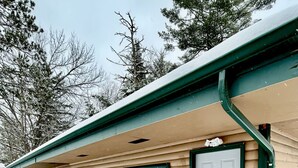A single-story building with a green roof and beige siding, featuring a door marked with the number 4 and a window with a wreath. - Moonlight Cottage | McKinney Lake Cottages | One Bedroom | One Bath (Grand Rapids)