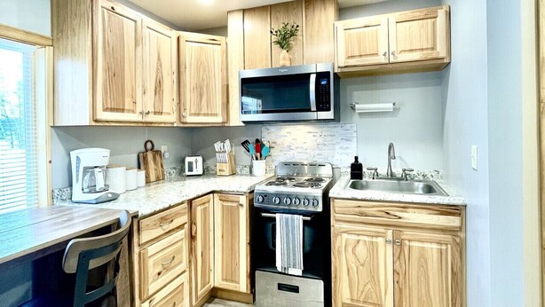 A compact kitchen with wooden cabinets, a microwave, a stove, and a sink. - Moonlight Cottage | McKinney Lake Cottages | One Bedroom | One Bath (Grand Rapids)