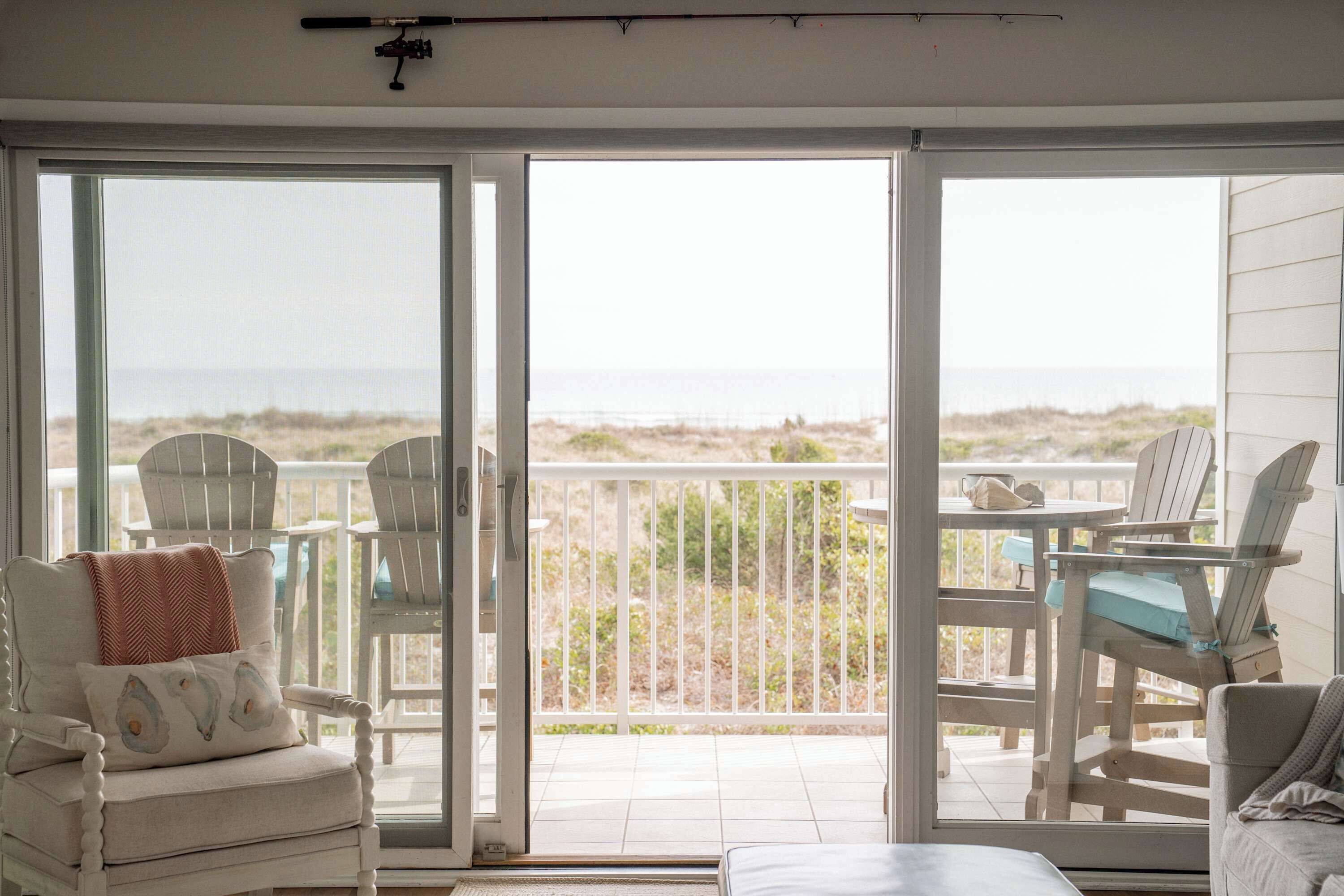 Habitació amb porta corredissa de vidre que dona a un balcó amb vista a la platja. Hi ha dues cadires blanques i una taula amb coixí blau.