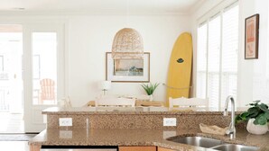 Una cocina moderna con encimeras de granito, electrodomésticos de acero inoxidable, armarios de madera y una tabla de surf en la pared.