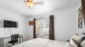 Un dormitorio con cama, escritorio, silla, televisor y ventana con cortinas.