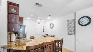Una cocina con encimera de granito, sillas de madera, un lavamanos blanco y un armario empotrado con adornos.