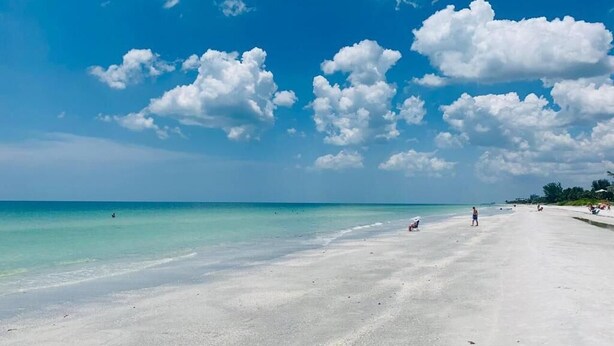 Una extensa playa arenosa con aguas turquesas cristalinas y nubes dispersas en el cielo.