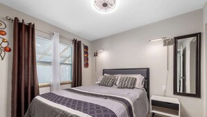 A bedroom with a bed, curtains, a bedside table, a mirror, and a ceiling fan. - 3 Min Walk to Beach | Modern Coastal Retreat (Indian Rocks Beach)