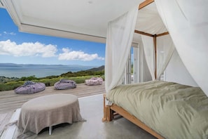 Ein Schlafzimmer mit Bett, Baldachin, Sitzsäcken und Meerblick.