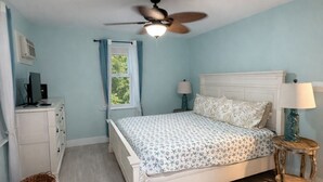 Een slaapkamer met een bed, een plafondventilator, een raam met gordijnen, een nachtkastje en een lamp.