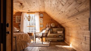 A cozy attic bedroom with a wooden sloped ceiling, a chandelier, a bed with a canopy, two wicker chairs, a small table, and a shelf with decorative items. - Special Price! Charming 4-bedroom Farmhouse w/Hot Tub in Peaceful Wears Valley (Sevierville)