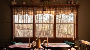 A cozy dining area with a table set for two, a bench, and a window with a forest view. - Special Price! Charming 4-bedroom Farmhouse w/Hot Tub in Peaceful Wears Valley (Sevierville)