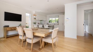 A modern kitchen with white cabinets, a wooden dining table, and six chairs. - Pet Friendly - Evergreen by the Bay (Sandringham)