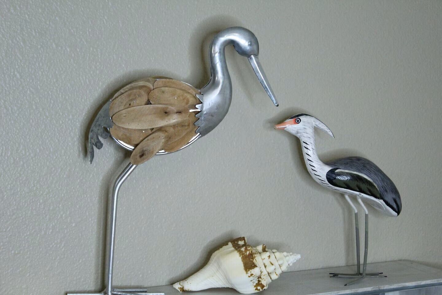 Une sculpture représentant une grue et un héron, posée sur une étagère avec un coquillage.