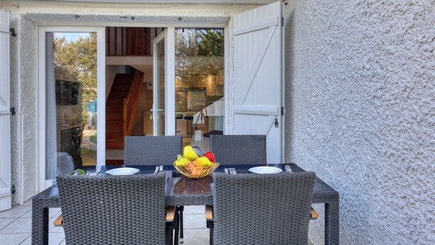 Un espace extérieur aménagé pour les repas, avec des meubles en osier et un panier de fruits.