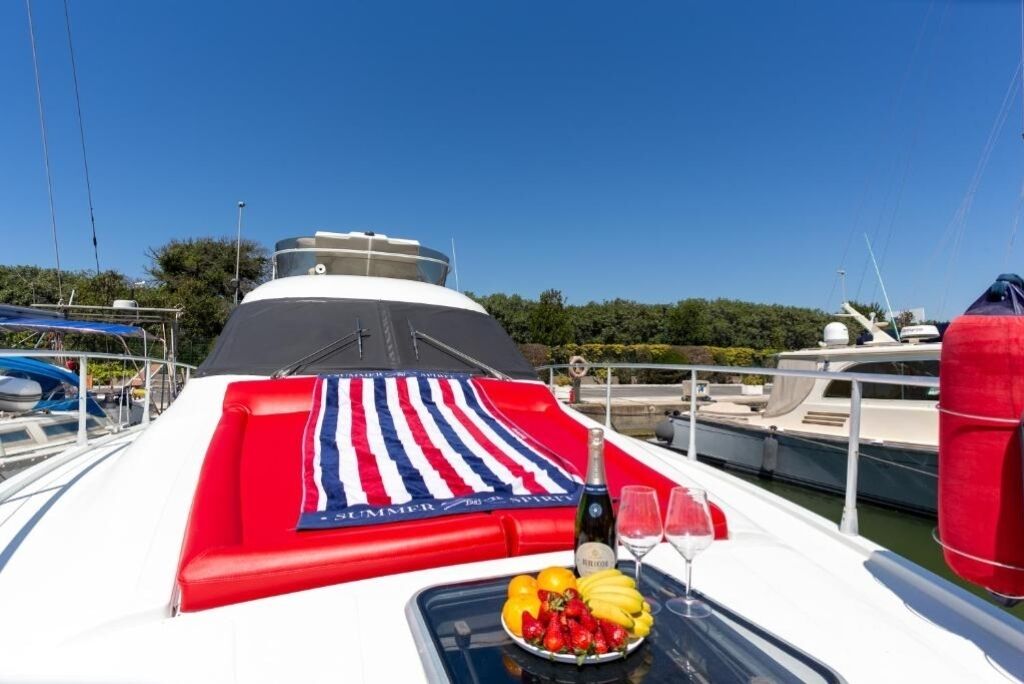 Cubierta de barco con un cubre franjas rojo y blanco, una botella de champán y un bol de fruta.