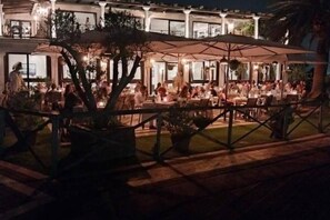 Un espace de restauration en plein air, avec des tables et des parasols, entouré d’une petite clôture et agrémenté de plantes en pot.