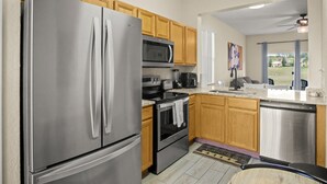 A modern kitchen with stainless steel appliances, wooden cabinets, and a view to the backyard. - Resort Style Family Friendly 4bd Near Disney (Davenport)