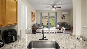 A kitchen with granite countertops, a built-in sink, wooden cabinets, a coffee maker, and a dining area with a table and chairs. - Resort Style Family Friendly 4bd Near Disney (Davenport)