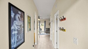 A hallway with a framed Mickey Mouse poster, a ceiling fan, and a door with a coat rack. - Resort Style Family Friendly 4bd Near Disney (Davenport)