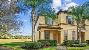 A two-story house with a beige exterior, a front door, and a small front yard with a lawn and a few trees. - Resort Style Family Friendly 4bd Near Disney (Davenport)