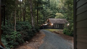 Eine Holzhütte mit einem Schotterweg, der zu einer Holzterrasse führt, umgeben von dichtem Wald.