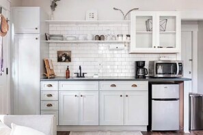 Une cuisine avec des meubles blancs, un four à micro-ondes, une machine à café et un réfrigérateur.