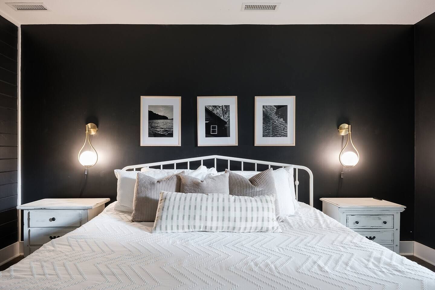 A bedroom with a white bed, two bedside tables, and three framed pictures on the wall.