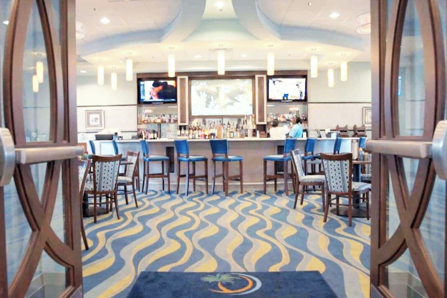 A bar area with multiple stools, a counter, and two televisions mounted on the wall.