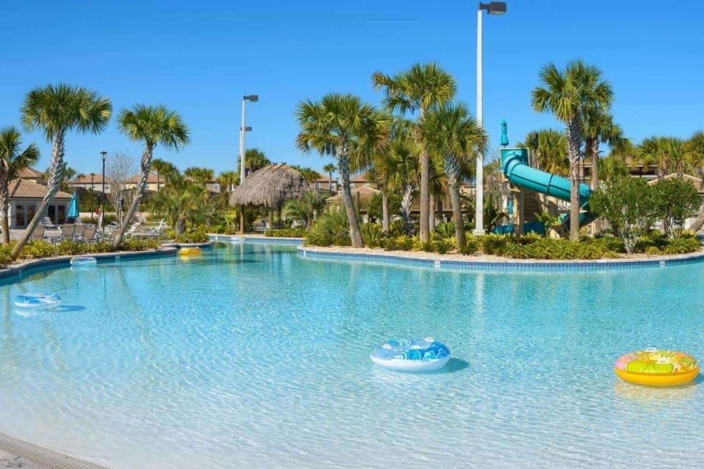 Une piscine d’un bleu éclatant, bordée de palmiers, avec un toboggan aquatique en arrière-plan.