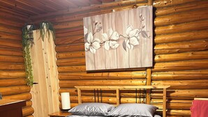 Ein Zimmer einer Holzhütte mit einem Bett, einem Nachttisch, einem roten Sessel und einem Wandbild.