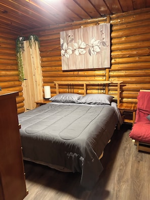 Une pièce de cabane en bois comprenant un lit, une table de chevet, une chaise rouge et un tableau accroché au mur.