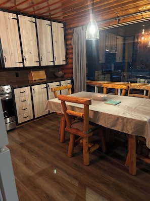 Une table à manger en bois avec des chaises, un coin cuisine avec des placards et une vue par la fenêtre.
