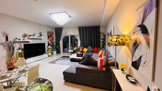 Una sala de estar moderna con un televisor de pantalla plana grande, un sofá con cojines, una mesa de centro y un comedor con una mesa preparada para dos.